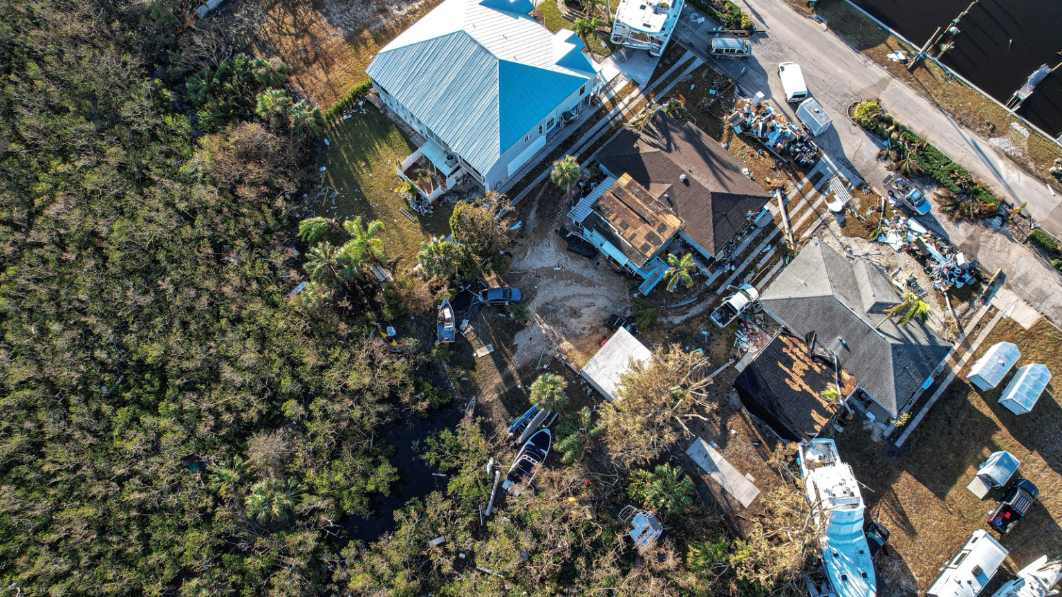 Aerial view of coastal neighborhood with storm damage, debris, and boats displaced by hurricane impact
